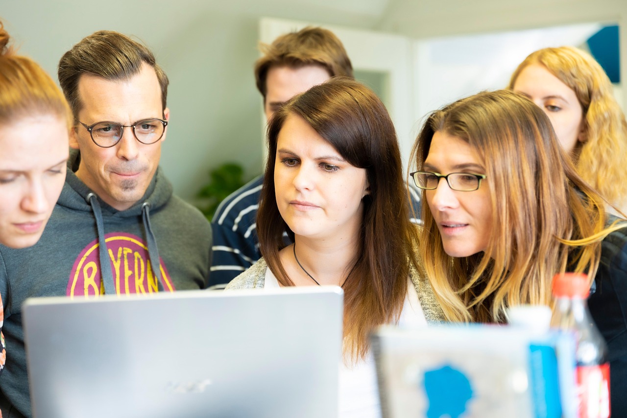 Eine gemischte Seminargruppe steht vor einem geöffneten Laptop